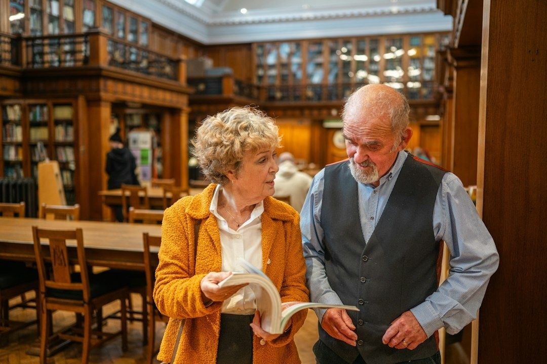 To eldre voksne snakker sammen med en bok i et bibliotek